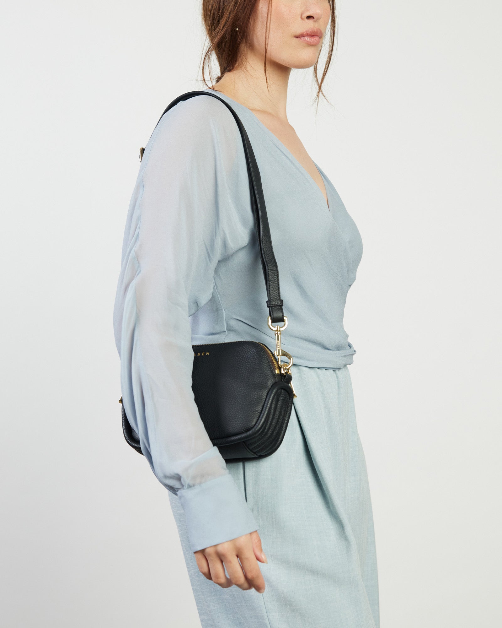 A black pebbled leather crossbody bag with pale gold hardware and a detachable strap, displayed against a white background.