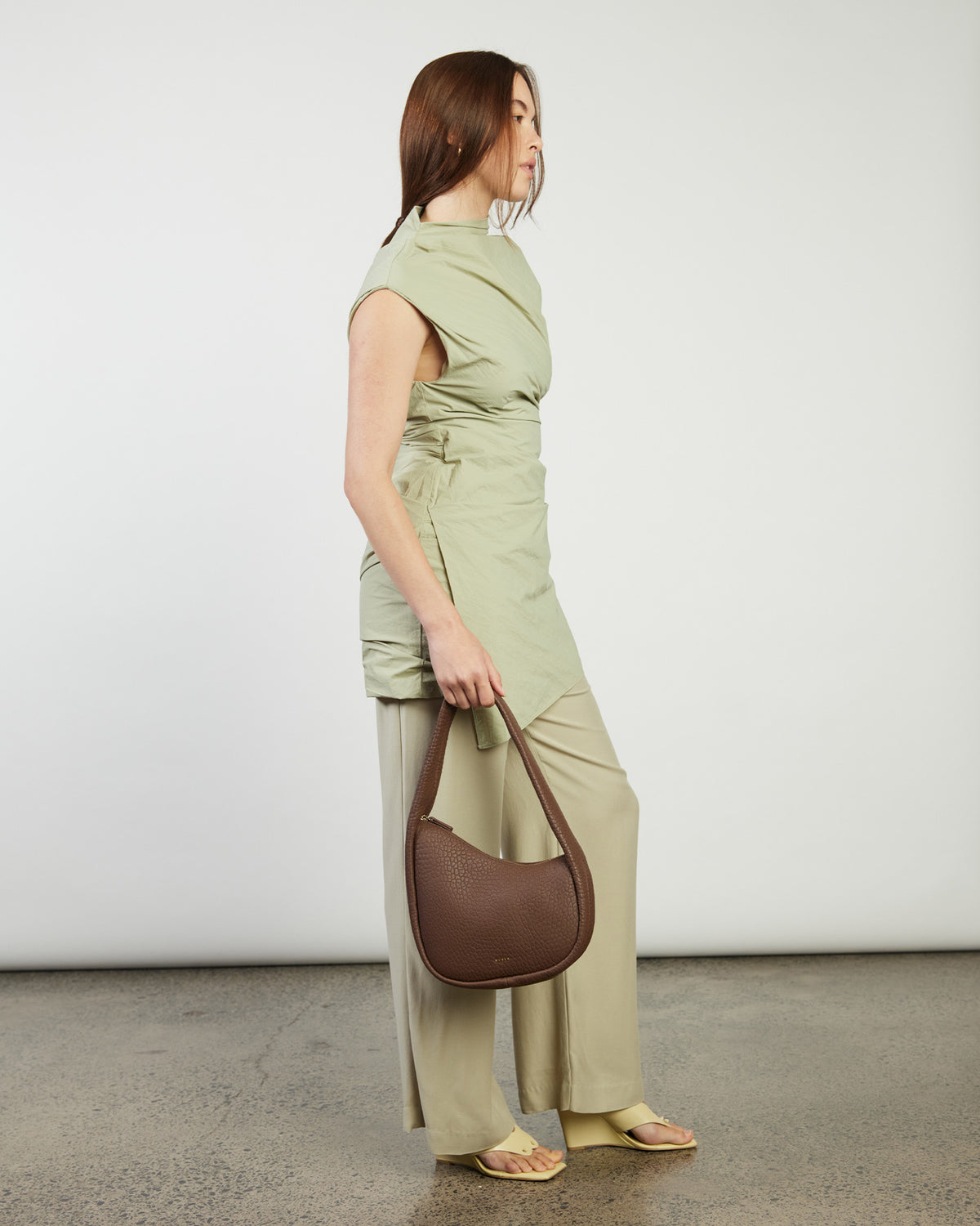 Woman in a green outfit holding a brown bag against a white background