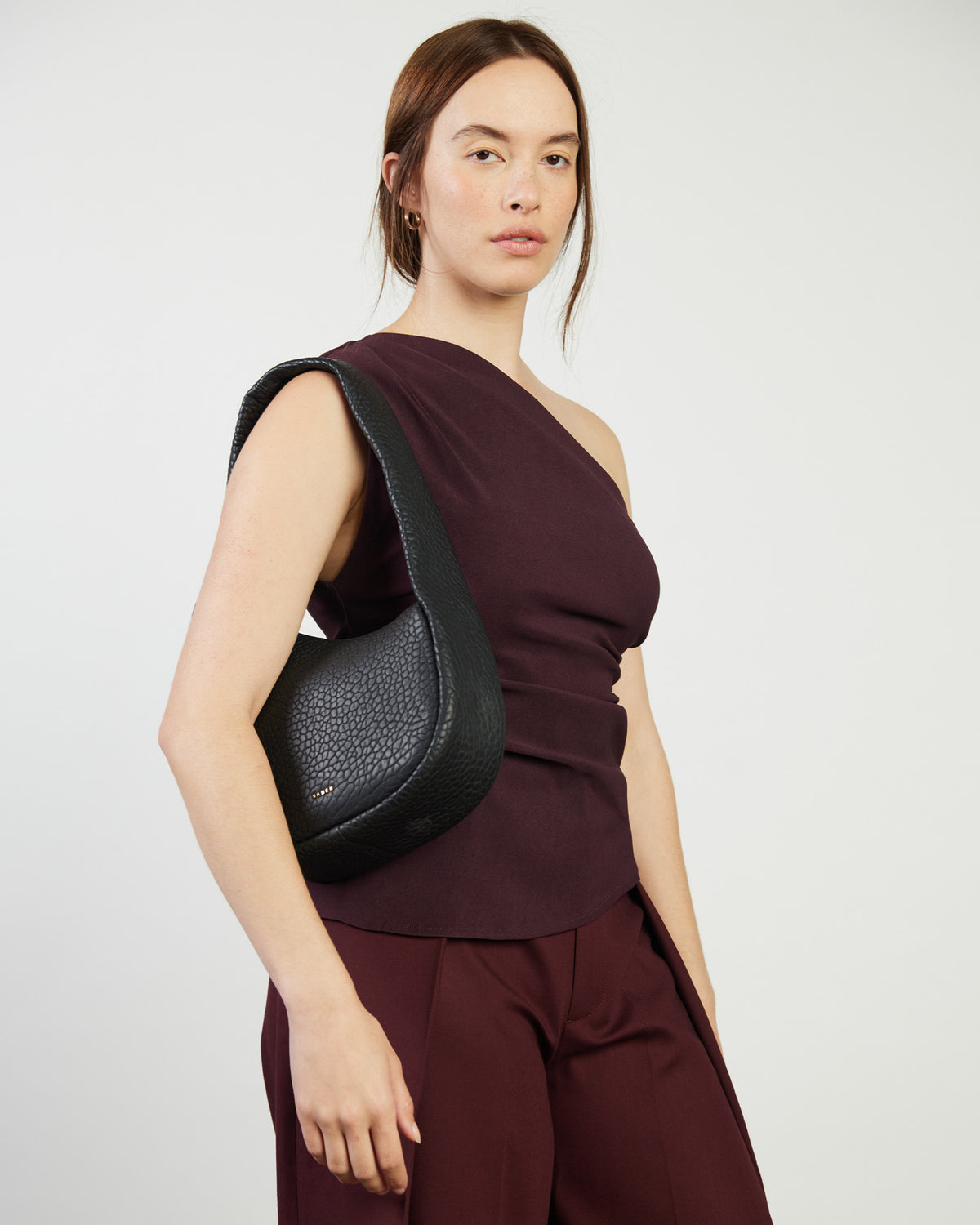 Woman wearing a black shoulder bag and burgundy outfit on a white background