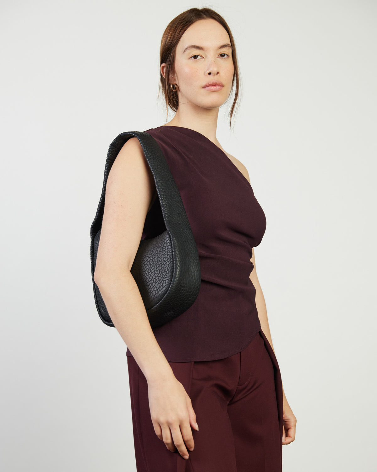 Woman wearing a dark red one-shoulder top and black bag against a white background
