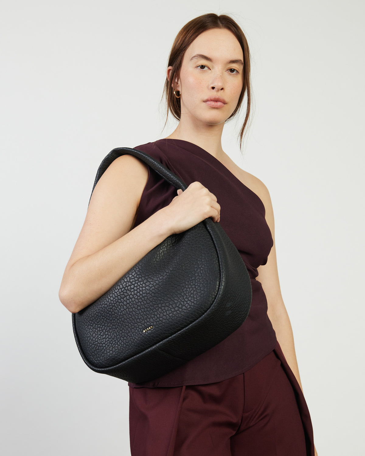 Woman holding a black handbag against a plain background