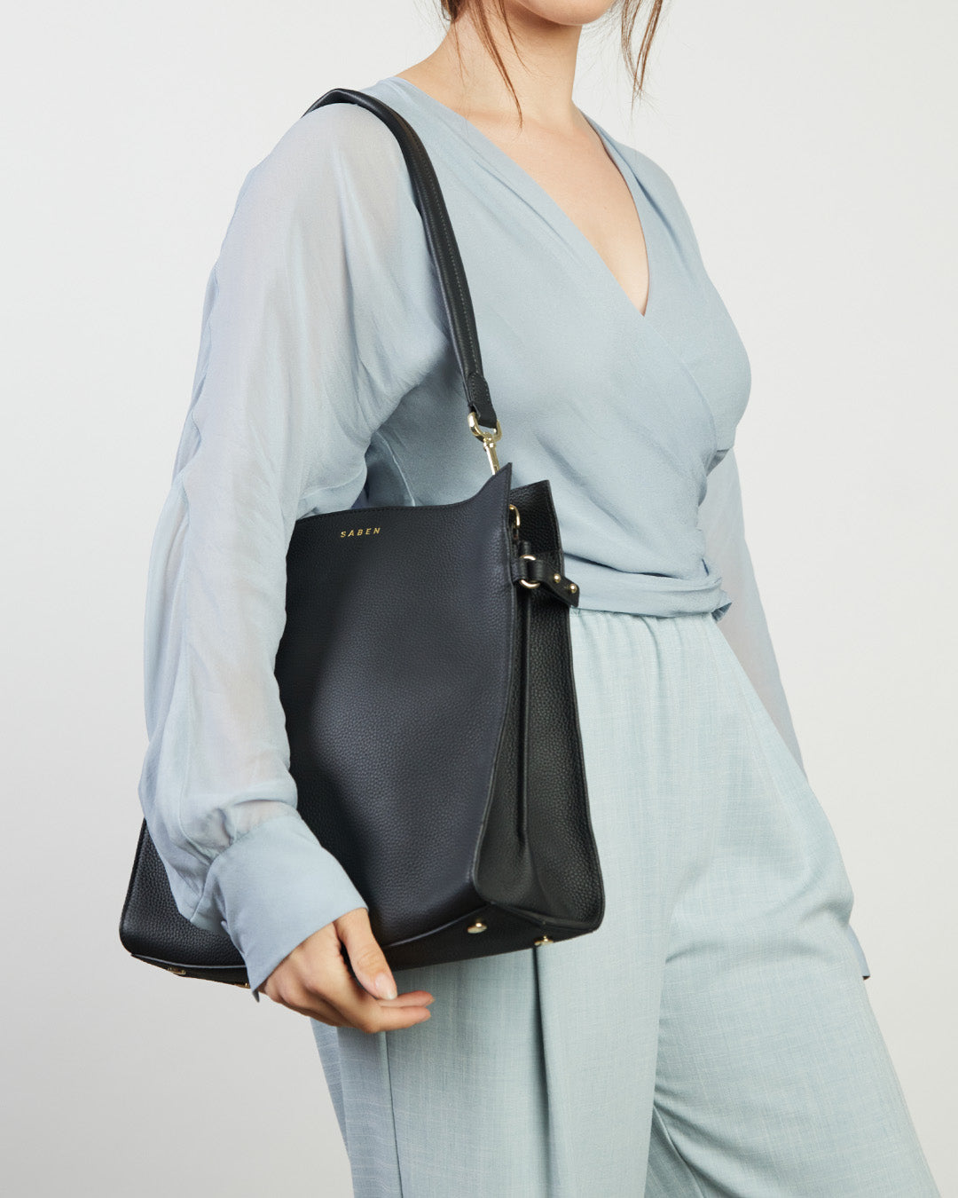 Person wearing a light blue outfit holding a black handbag against a plain background