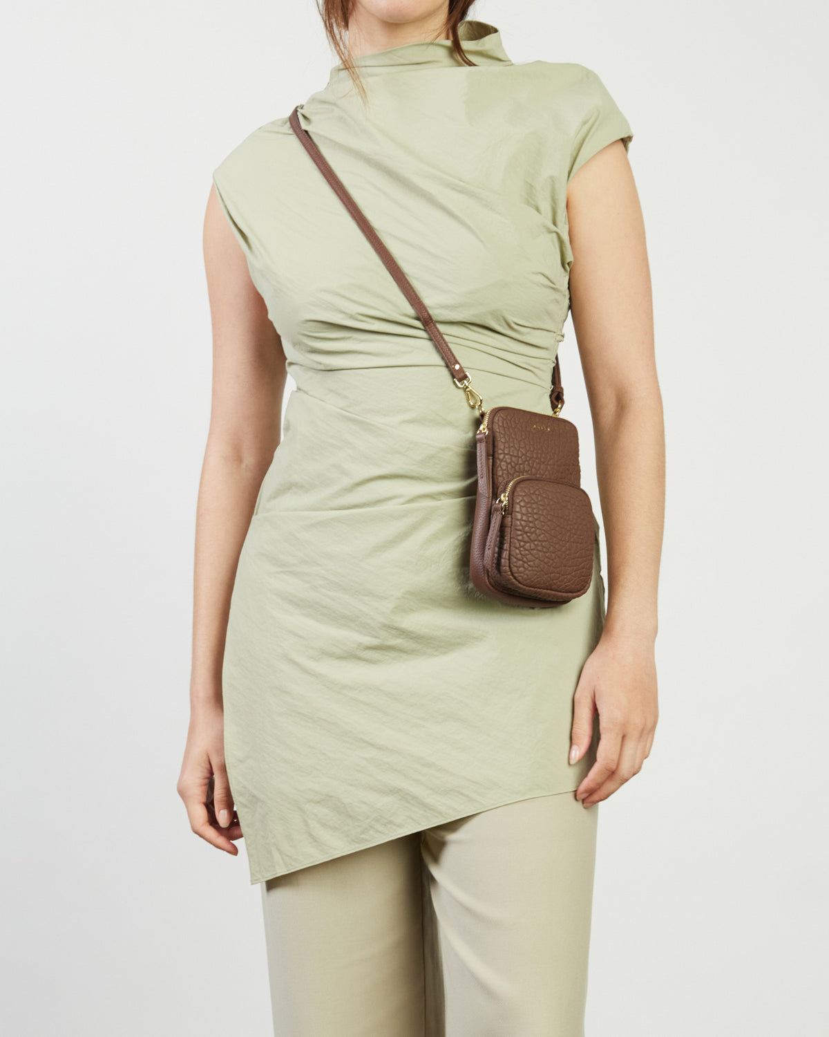 Woman wearing a green dress with a brown crossbody bag on a light gray background
