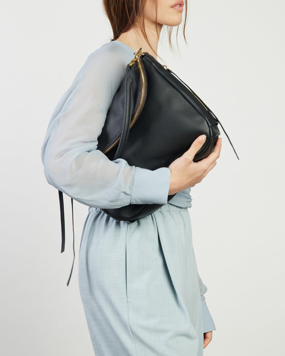 Person holding a black leather bag against a plain background