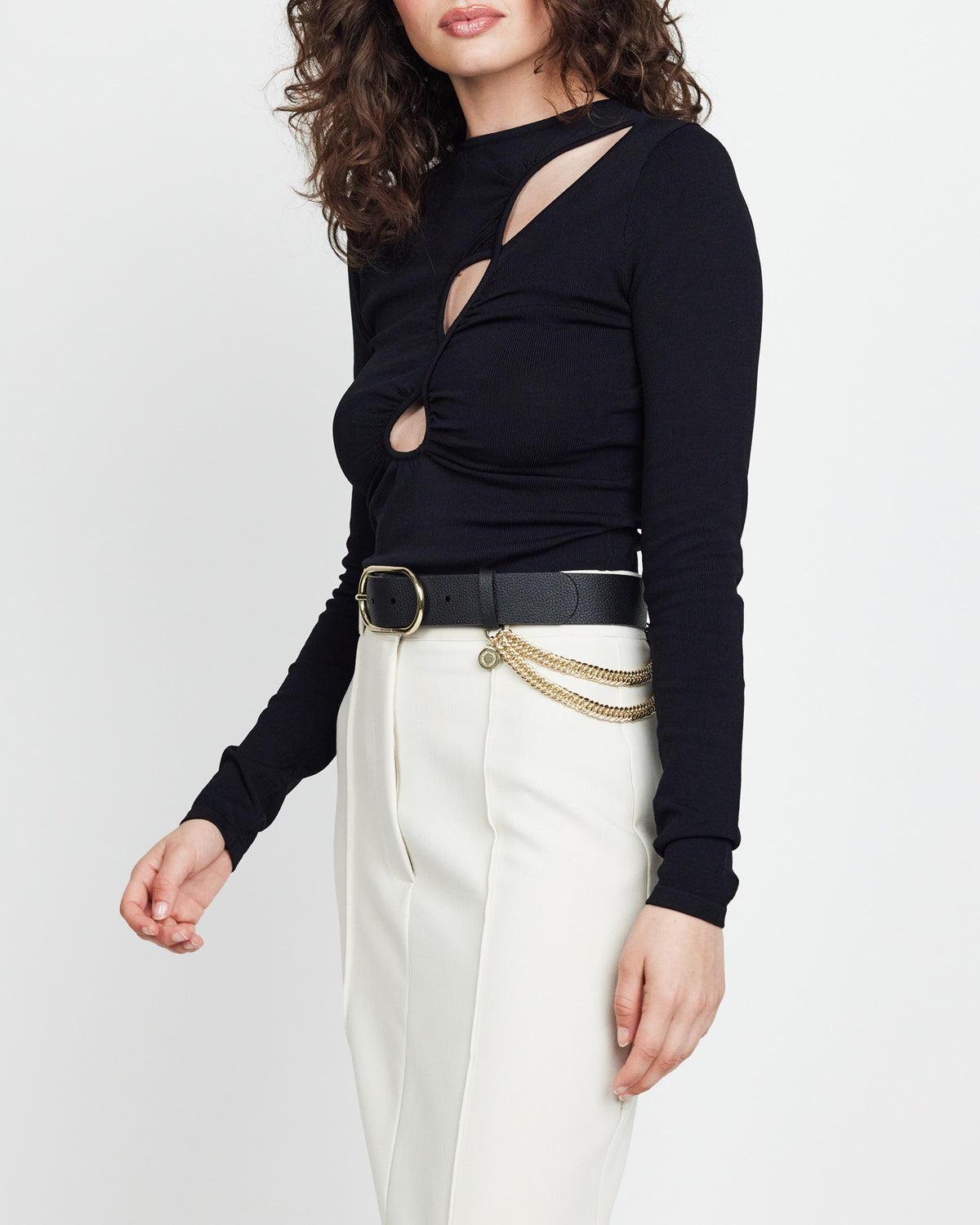 Person wearing a black long-sleeve top with cut-out design and white pants on a plain background