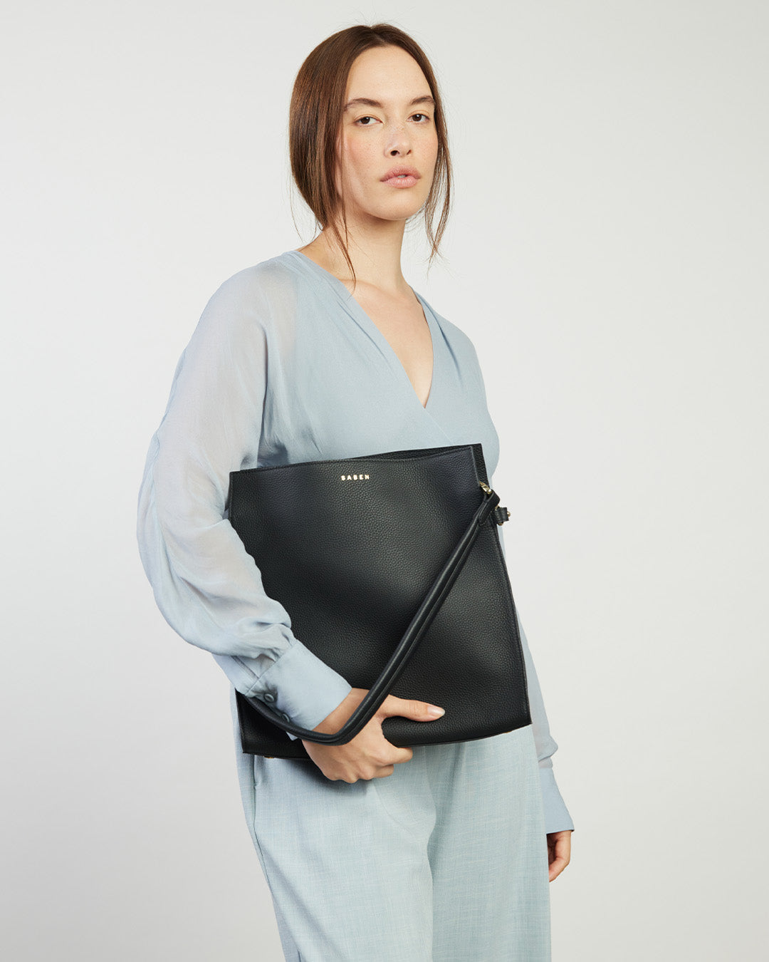 Woman holding a black clutch bag against a plain background