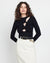 Woman wearing a black long-sleeve top with cut-out design and white pants on a plain background