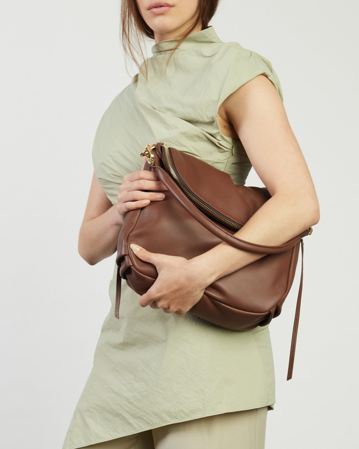 Woman holding a brown leather bag against a plain background