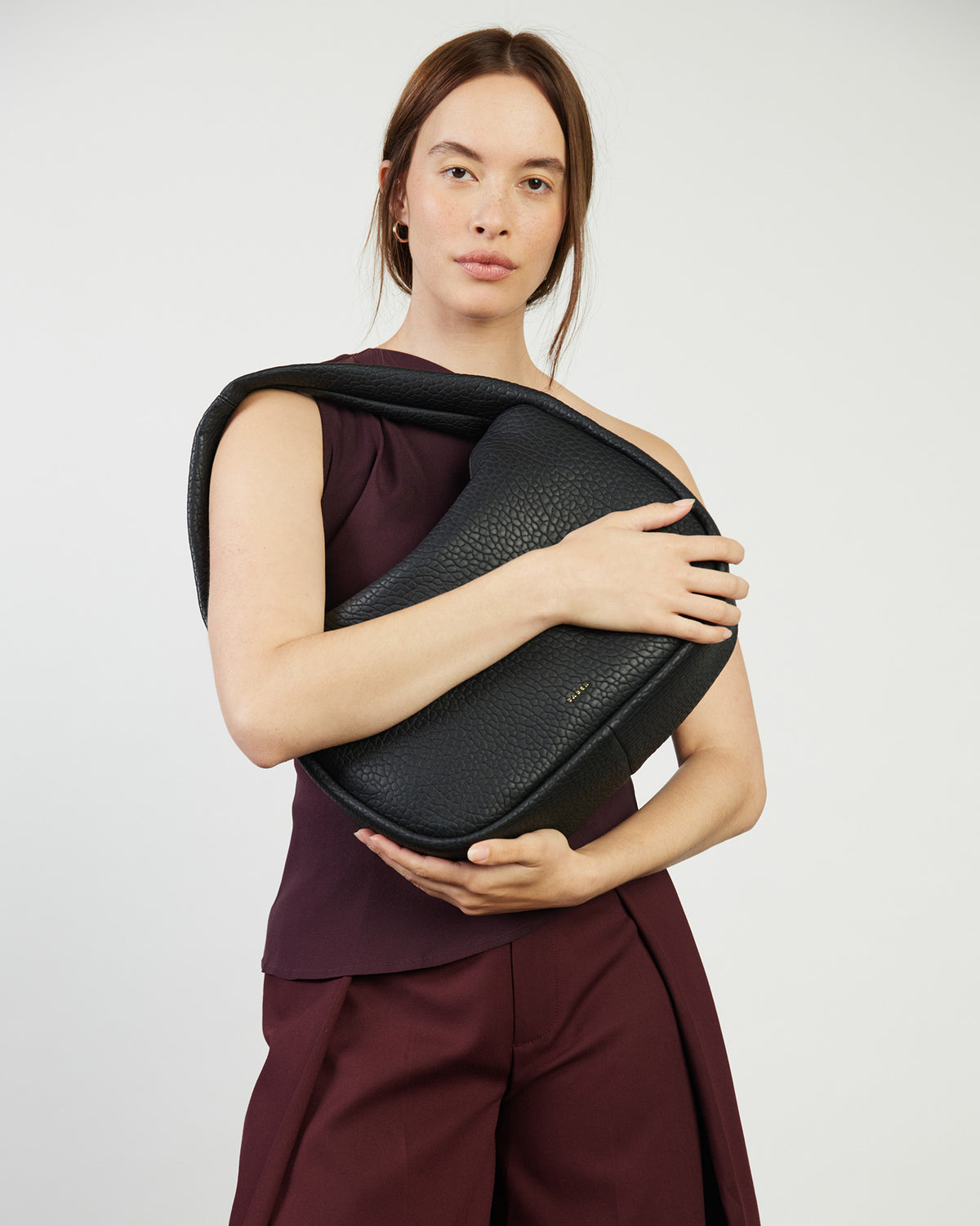 Woman holding a black leather bag against a plain background