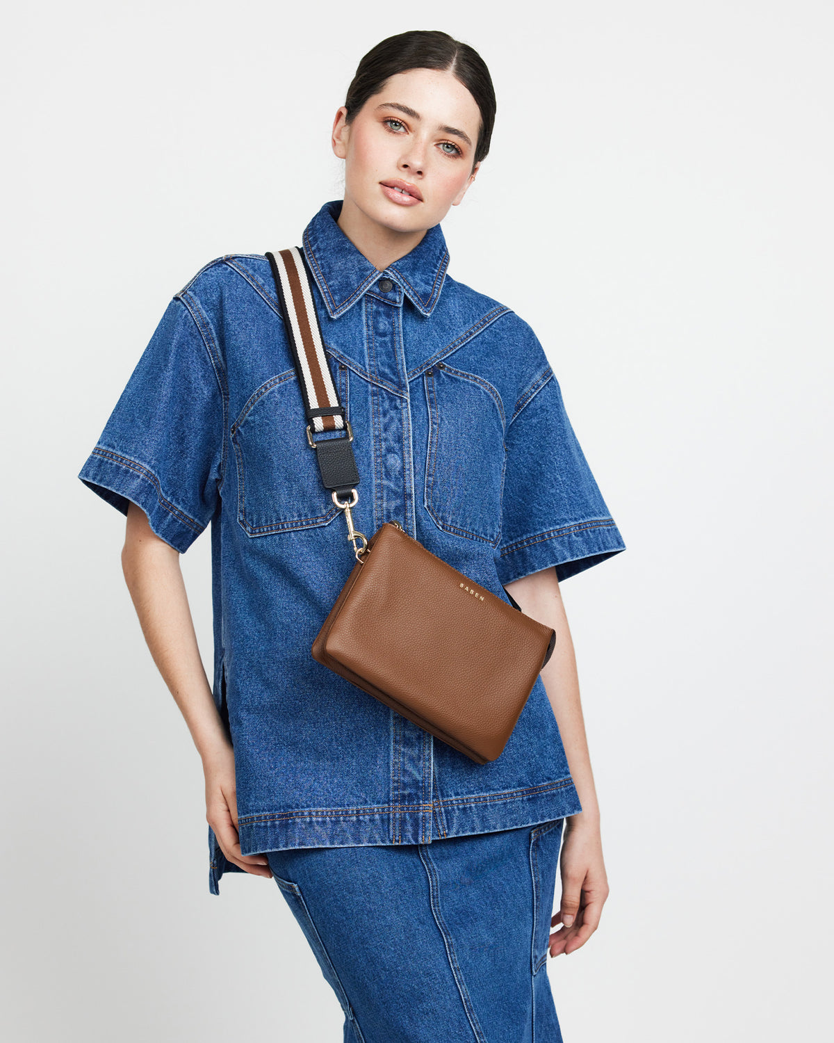 Person wearing a denim outfit with a brown bag on a plain background
