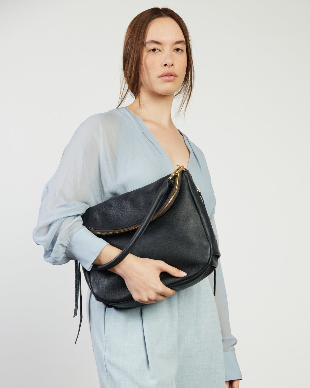 Woman holding a black leather bag against a plain background